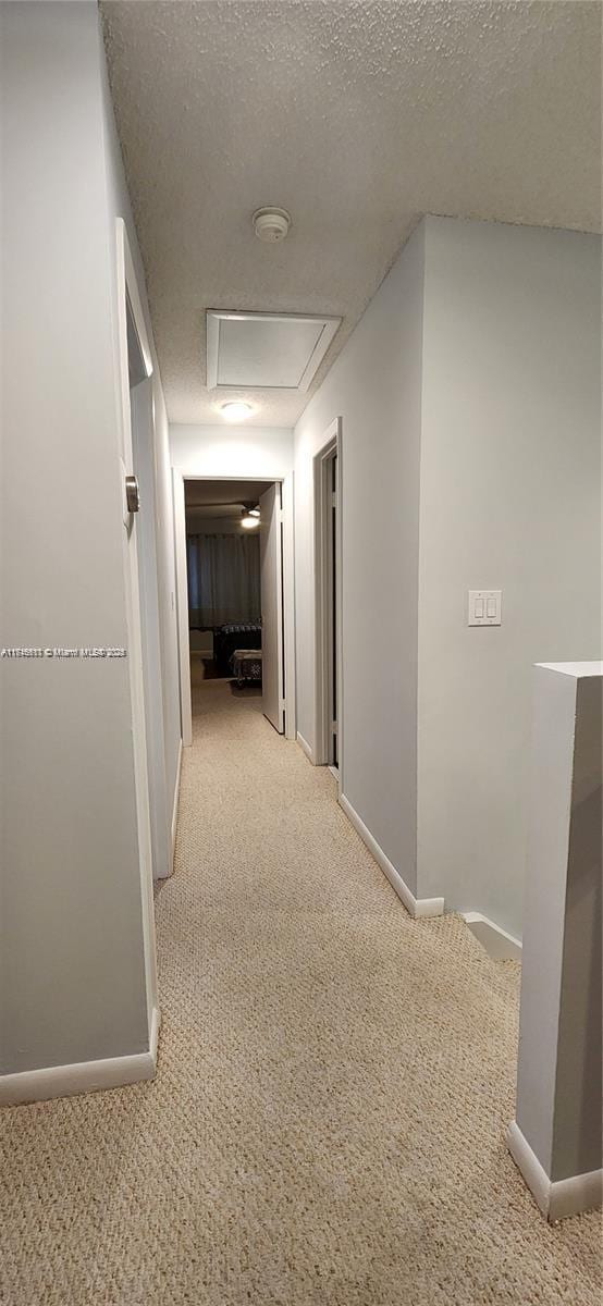 hallway with light carpet and a textured ceiling