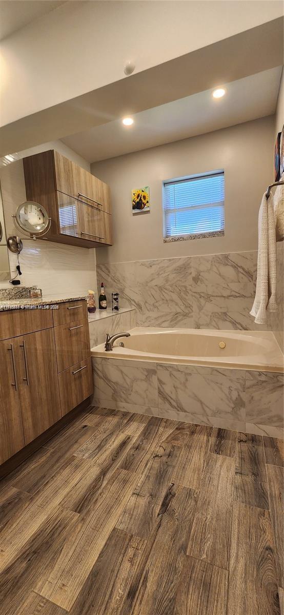 bathroom with hardwood / wood-style floors, vanity, and tiled bath