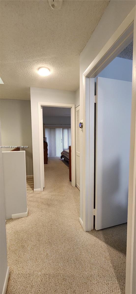 hallway with a textured ceiling and light colored carpet