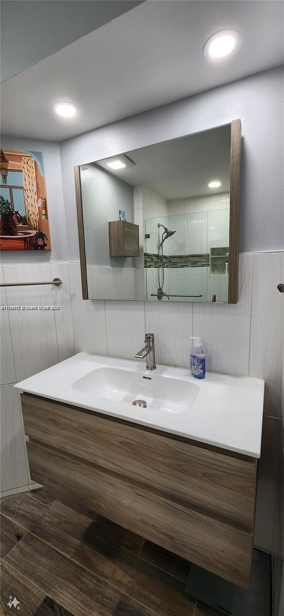 bathroom with a tile shower, vanity, and tile walls