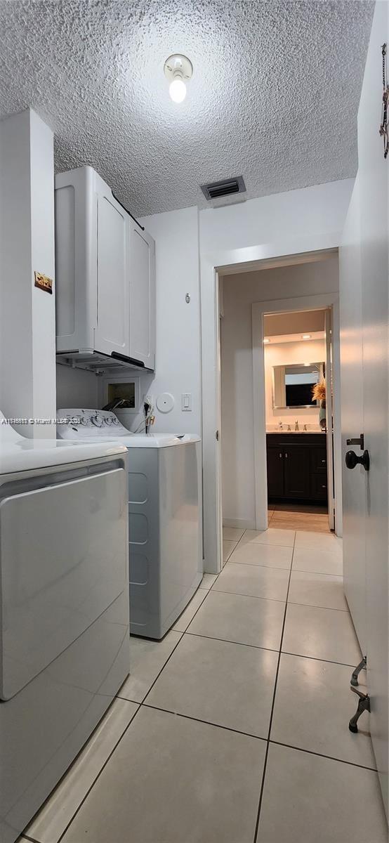 laundry room with washer and dryer, light tile patterned flooring, cabinets, and a textured ceiling