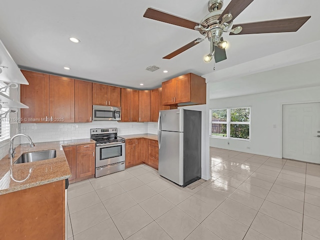 kitchen with sink, light tile patterned floors, appliances with stainless steel finishes, light stone countertops, and backsplash