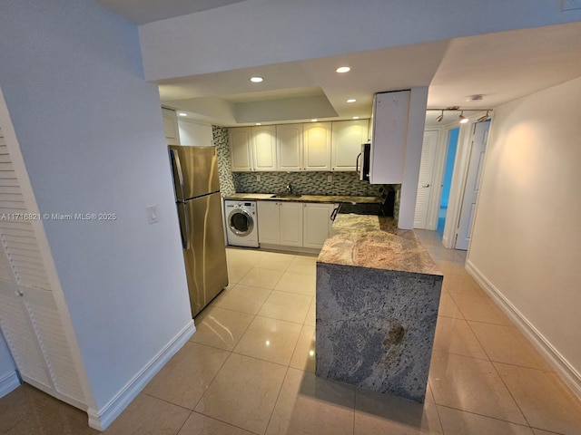 kitchen with backsplash, light tile patterned floors, washer / dryer, white cabinetry, and stainless steel refrigerator