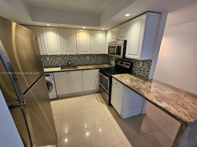 kitchen featuring sink, stainless steel appliances, light tile patterned floors, washer / dryer, and white cabinets