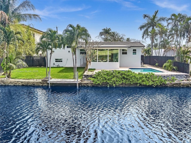 back of property with a sunroom, a water view, a fenced in pool, and a lawn