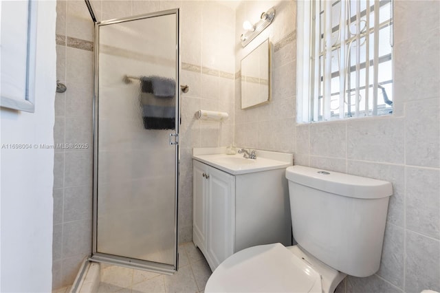 bathroom with tile patterned flooring, toilet, a shower with door, vanity, and tile walls