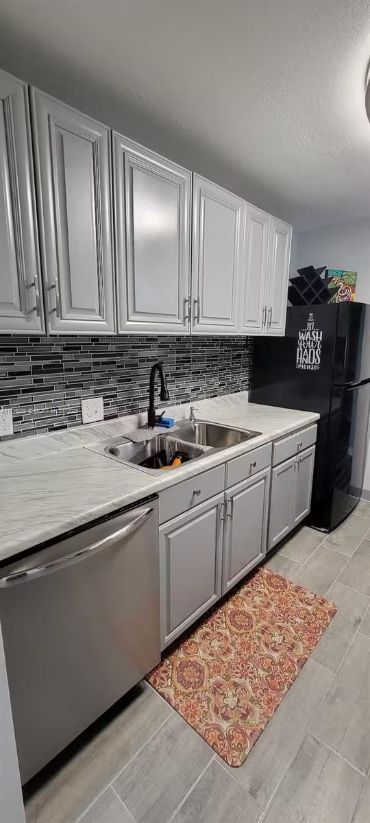 kitchen featuring decorative backsplash, black fridge, gray cabinetry, sink, and dishwasher