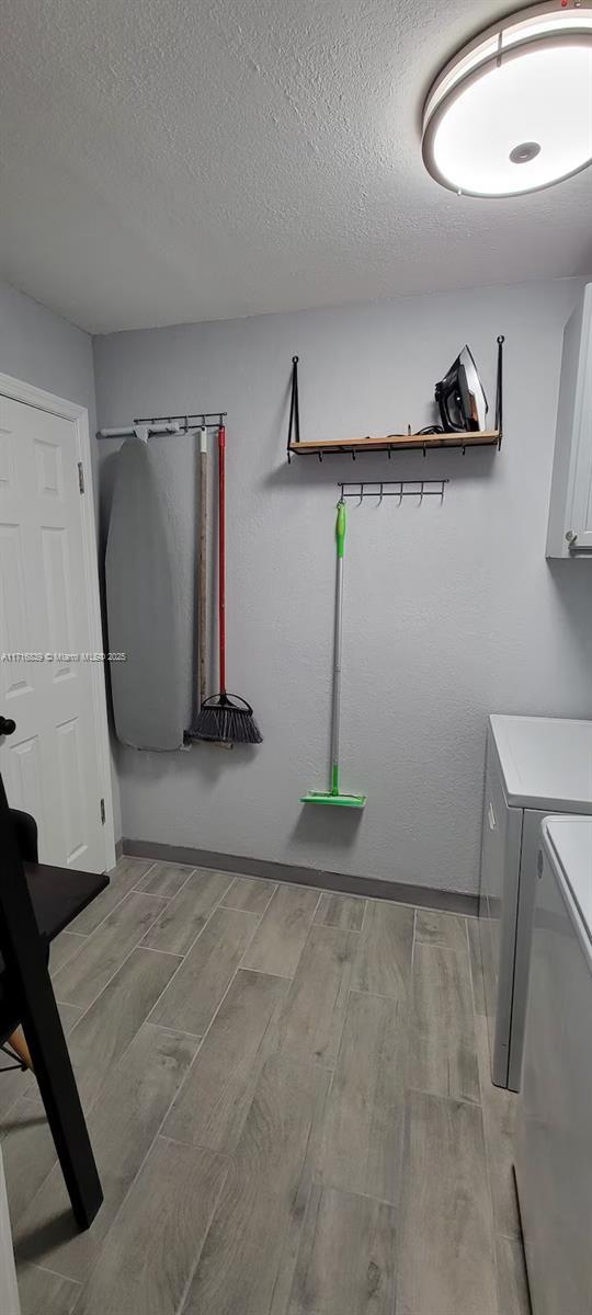 clothes washing area with cabinets, separate washer and dryer, and a textured ceiling