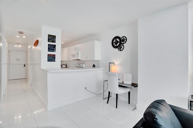 kitchen with kitchen peninsula, stove, sink, light tile patterned floors, and white cabinetry