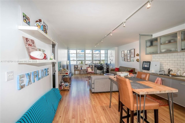 dining area featuring floor to ceiling windows, sink, rail lighting, and light hardwood / wood-style flooring