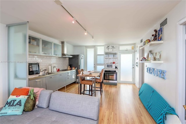 kitchen with white microwave, visible vents, backsplash, wall chimney exhaust hood, and glass insert cabinets