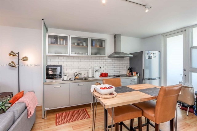 kitchen with decorative backsplash, black electric stovetop, wall chimney exhaust hood, light hardwood / wood-style floors, and stainless steel refrigerator