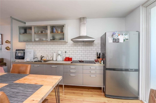 kitchen with glass insert cabinets, freestanding refrigerator, range hood, black electric stovetop, and gray cabinets