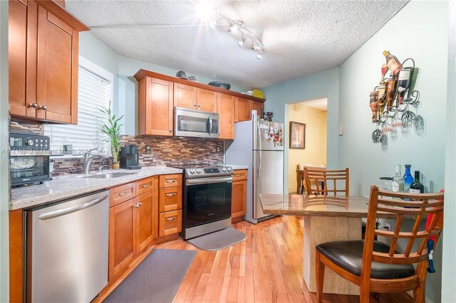 kitchen with appliances with stainless steel finishes, backsplash, light stone counters, sink, and light hardwood / wood-style floors