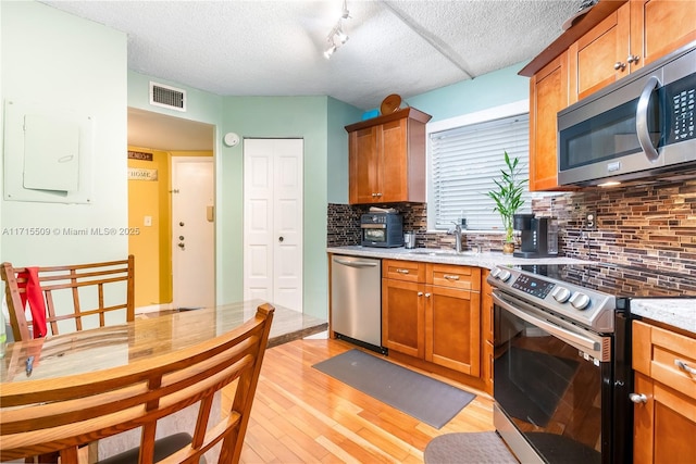 kitchen featuring light stone countertops, sink, stainless steel appliances, light hardwood / wood-style flooring, and backsplash