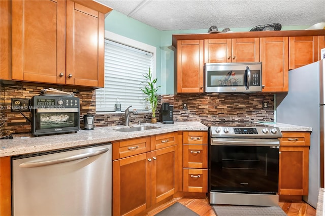 kitchen featuring light stone counters, sink, appliances with stainless steel finishes, and light hardwood / wood-style flooring