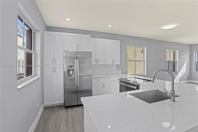 kitchen featuring white cabinetry, sink, stainless steel fridge, and light stone countertops