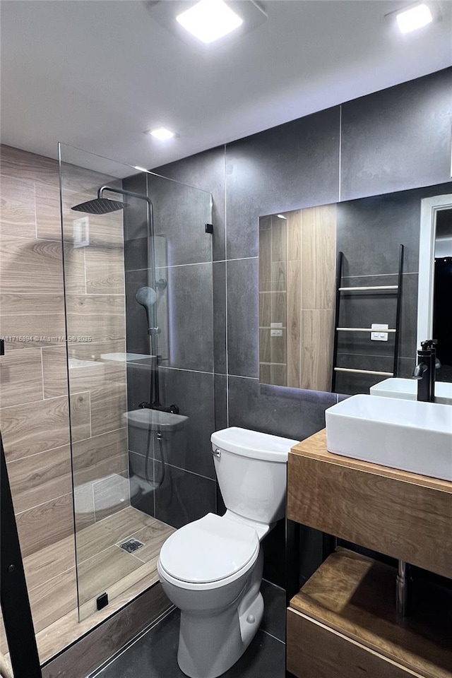 bathroom with a tile shower, vanity, toilet, and tile walls