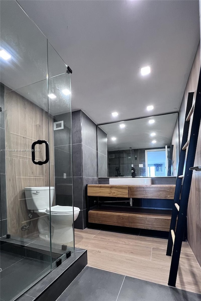 bathroom featuring walk in shower, tile patterned flooring, toilet, vanity, and tile walls