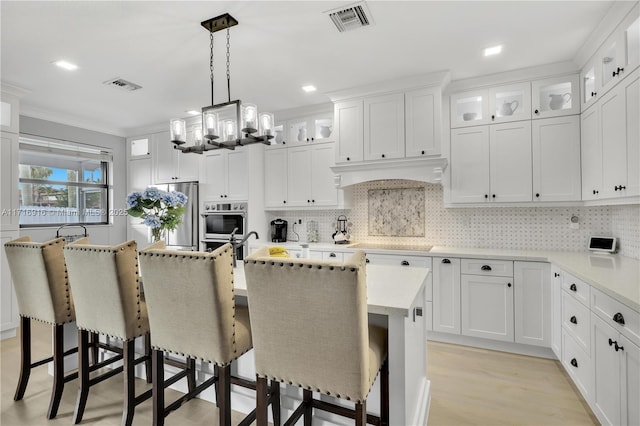 kitchen with hanging light fixtures, an island with sink, a breakfast bar area, white cabinets, and custom exhaust hood