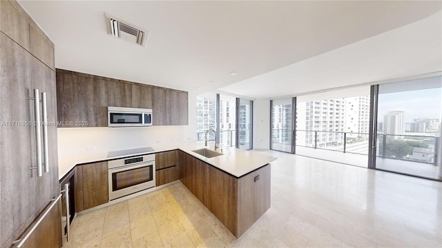 kitchen with sink, expansive windows, kitchen peninsula, stainless steel appliances, and light wood-type flooring