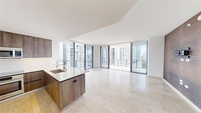 kitchen with sink, a wall of windows, black electric stovetop, stainless steel oven, and kitchen peninsula