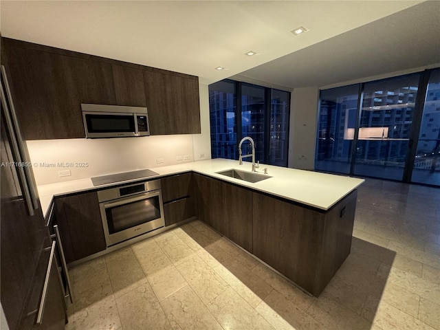 kitchen featuring dark brown cabinetry, sink, black appliances, and kitchen peninsula