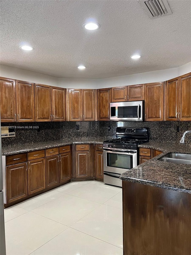 kitchen featuring sink, light tile patterned floors, dark stone counters, and appliances with stainless steel finishes