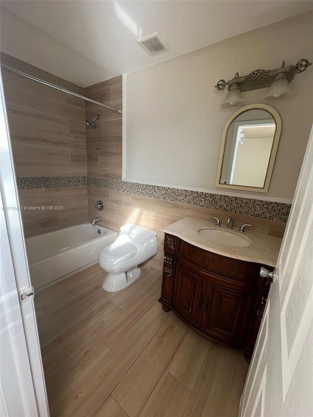 full bathroom with vanity, tiled shower / bath, hardwood / wood-style flooring, toilet, and tile walls