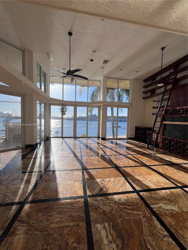 interior space with a textured ceiling, a towering ceiling, ceiling fan, and a water view