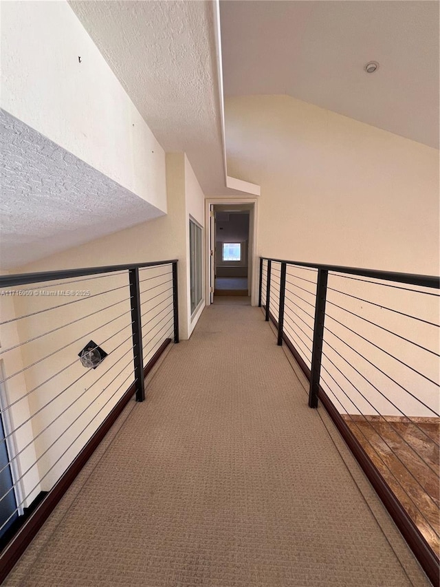 hallway featuring vaulted ceiling, light colored carpet, and a textured ceiling