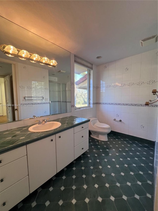 bathroom featuring vanity, toilet, a shower with door, and tile walls