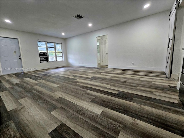 unfurnished living room featuring a barn door and dark wood-type flooring