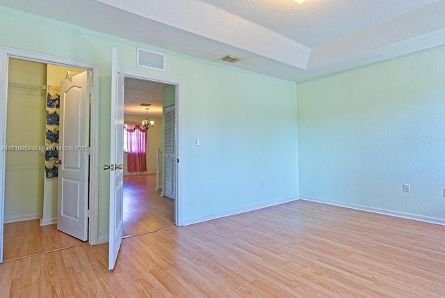 empty room featuring an inviting chandelier, light wood-type flooring, and a textured ceiling