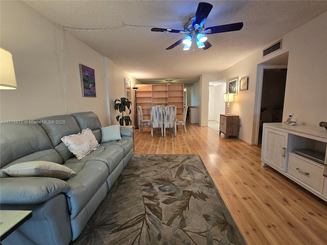 living room with ceiling fan, a textured ceiling, and light wood-type flooring