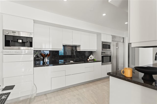 kitchen featuring tasteful backsplash, built in appliances, white cabinets, and dark stone counters