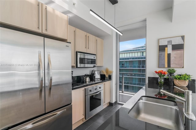 kitchen featuring dark countertops, light brown cabinets, decorative light fixtures, stainless steel appliances, and a sink