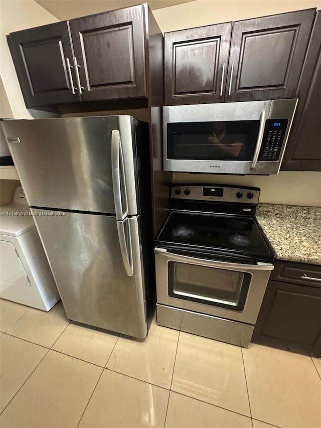 kitchen featuring dark brown cabinetry, light tile patterned floors, stainless steel appliances, and washer / dryer