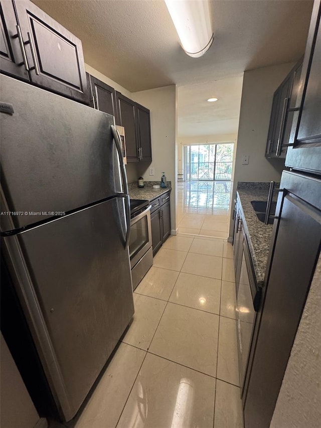 kitchen with a textured ceiling, dark stone countertops, light tile patterned floors, and stainless steel appliances