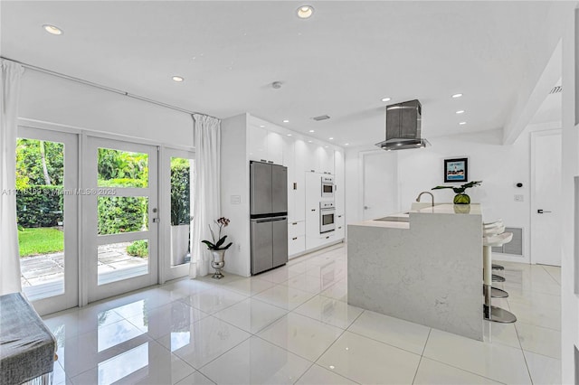 kitchen with white cabinetry, sink, island exhaust hood, stainless steel fridge, and light tile patterned floors