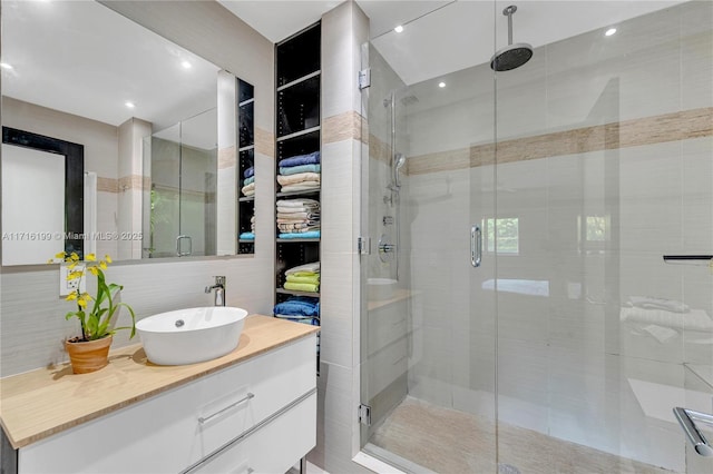 bathroom featuring backsplash, vanity, a shower with shower door, and tile walls