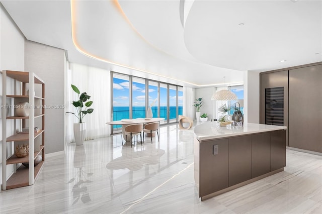 kitchen with expansive windows, dark brown cabinets, a water view, a center island, and hanging light fixtures