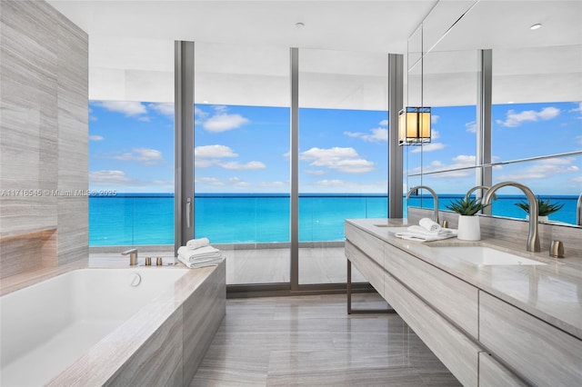 bathroom with a relaxing tiled tub, expansive windows, a water view, and vanity