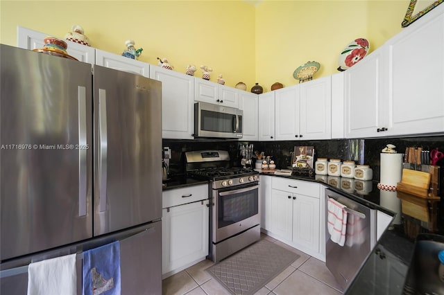 kitchen featuring dark countertops, backsplash, white cabinetry, appliances with stainless steel finishes, and light tile patterned flooring