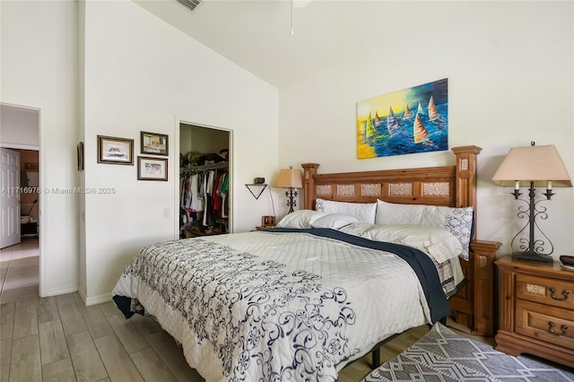 bedroom with wood finished floors, baseboards, high vaulted ceiling, a spacious closet, and a closet