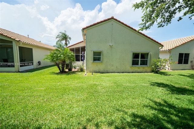 rear view of property featuring a tile roof, a yard, a sunroom, and stucco siding