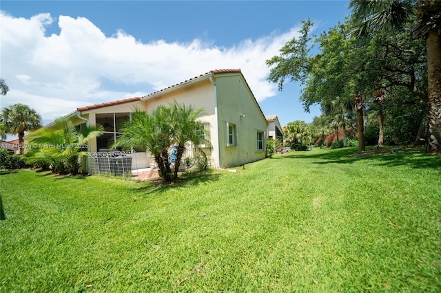 view of home's exterior with stucco siding, a tiled roof, a yard, and a sunroom