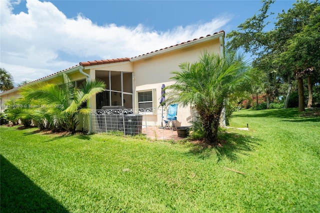 back of house with stucco siding, a lawn, a tile roof, a sunroom, and a patio area