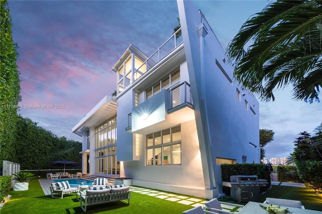 back house at dusk featuring a yard, a balcony, and a fenced in pool