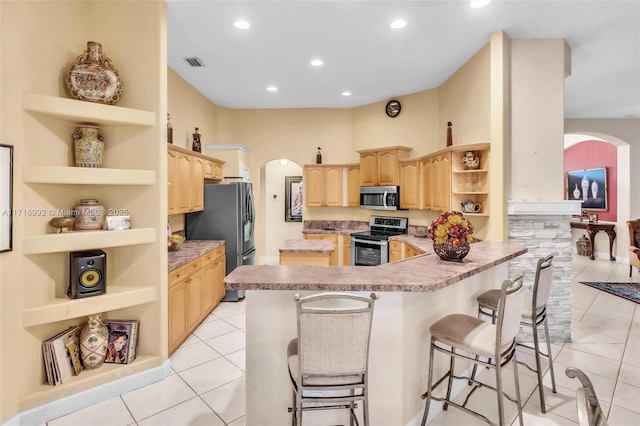 kitchen featuring a breakfast bar area, light tile patterned floors, light brown cabinetry, kitchen peninsula, and stainless steel appliances